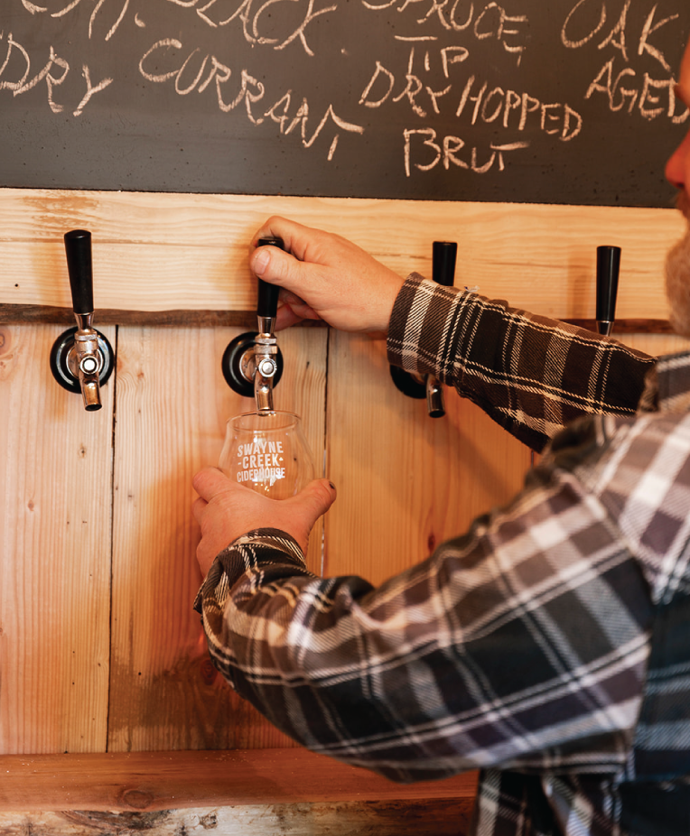 Bartender arms and hands close up pouring cider in the Swayne Creek Ciderhouse barn